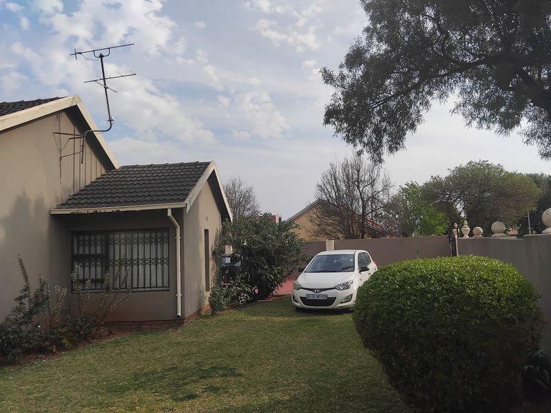 Front view of a residential house featuring a tiled roof, security bars on windows, and a surrounding boundary wall with a lawn area.