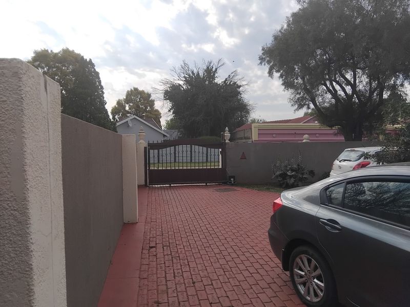 Front entrance view featuring a paved driveway, boundary wall, and metal security gate.