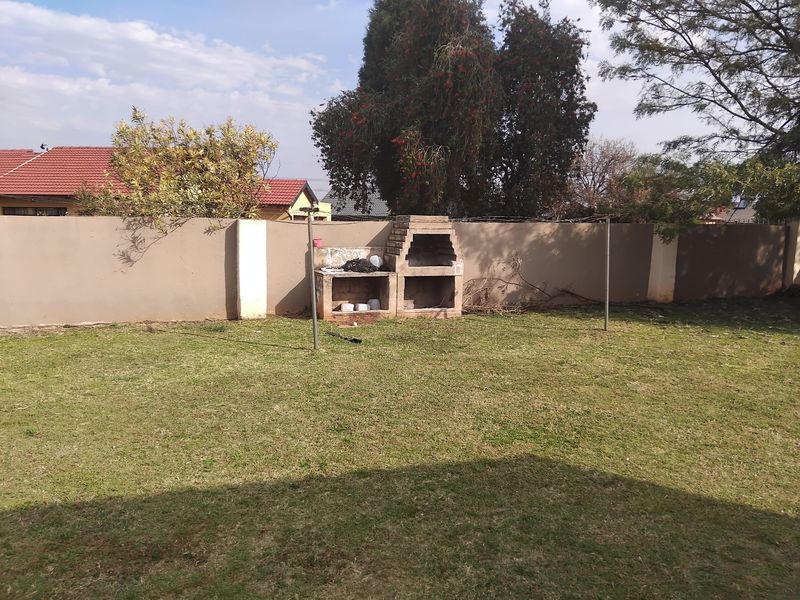 A spacious backyard featuring a grass lawn, a perimeter boundary wall, and a built-in brick braai area.
