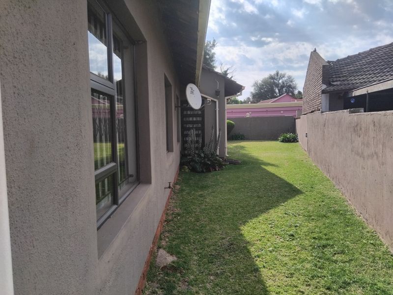 A view of the rear exterior of the house featuring a lawn, plastered boundary walls, and aluminium window frames.
