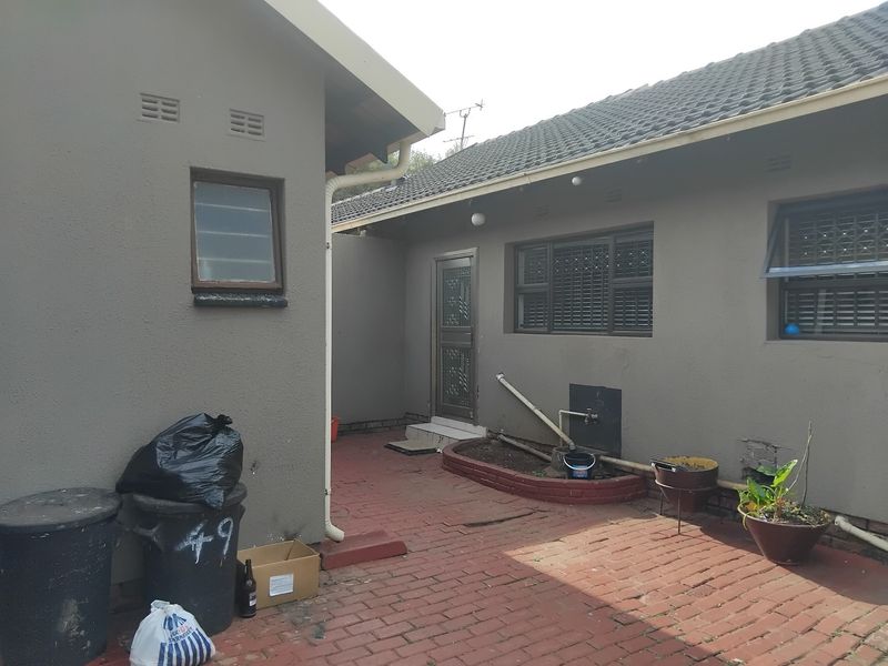 Rear exterior view of the property featuring brick paving, a security gate, and tiled roofing with external plumbing fixtures.