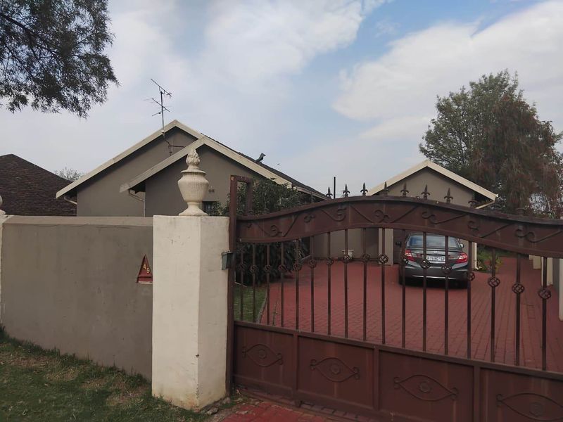 Front view of the property featuring a secure wrought iron gate, paved driveway, and boundary wall with a neutral exterior finish.