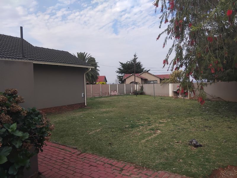 A spacious rear garden featuring a paved patio area, a built-in braai, and a perimeter boundary wall.