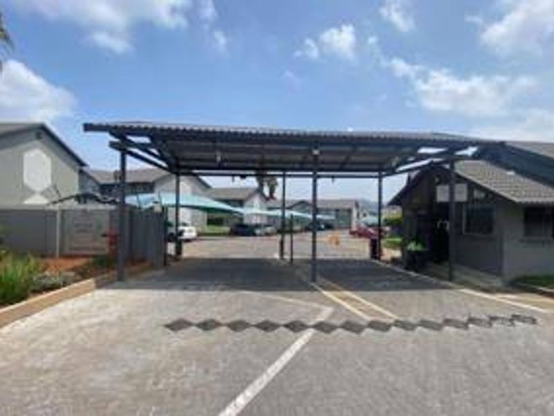 The entrance to the townhouse complex features a secure gated access point with a covered carport and paved driveway.