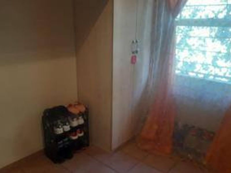 A bedroom featuring tiled flooring and a built-in cupboard, with natural light entering through a window fitted with security bars.