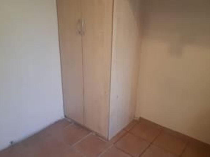 A simple bedroom featuring tiled flooring and a built-in wooden cupboard, offering a clean and functional space.