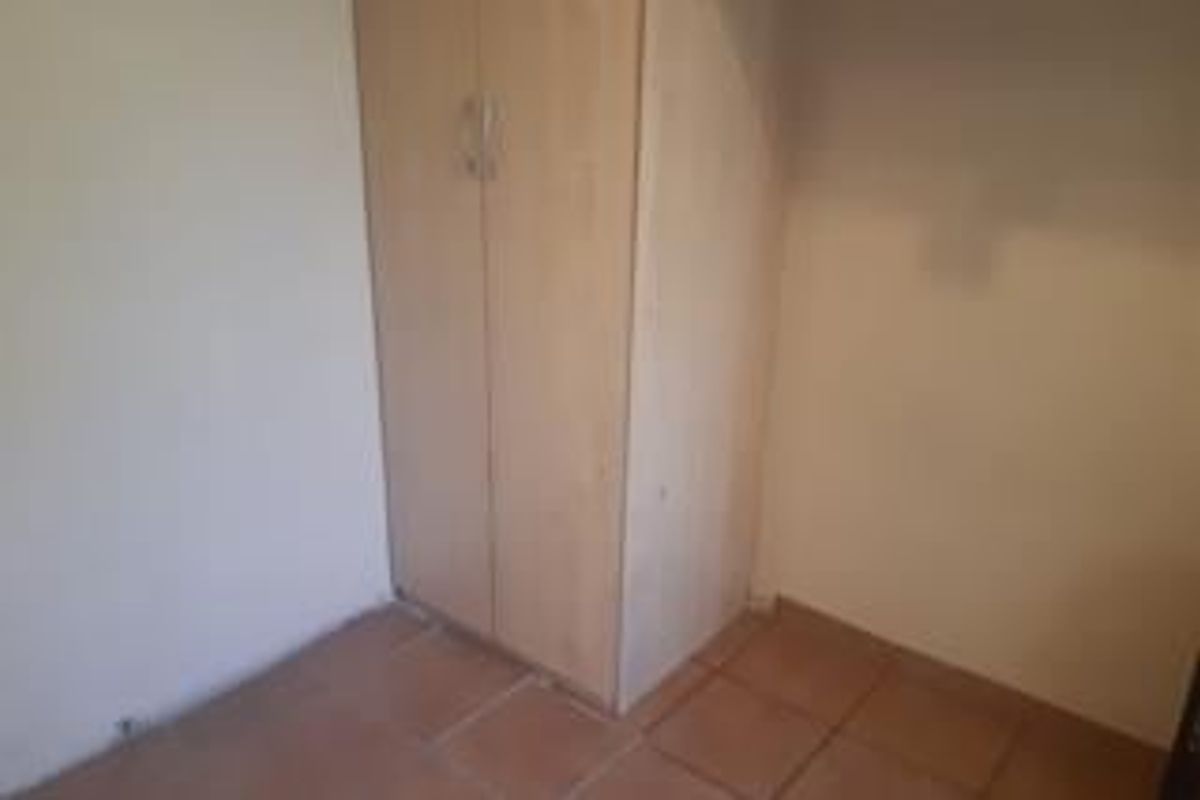 A simple bedroom featuring tiled flooring and a built-in wooden cupboard, offering a clean and functional space.