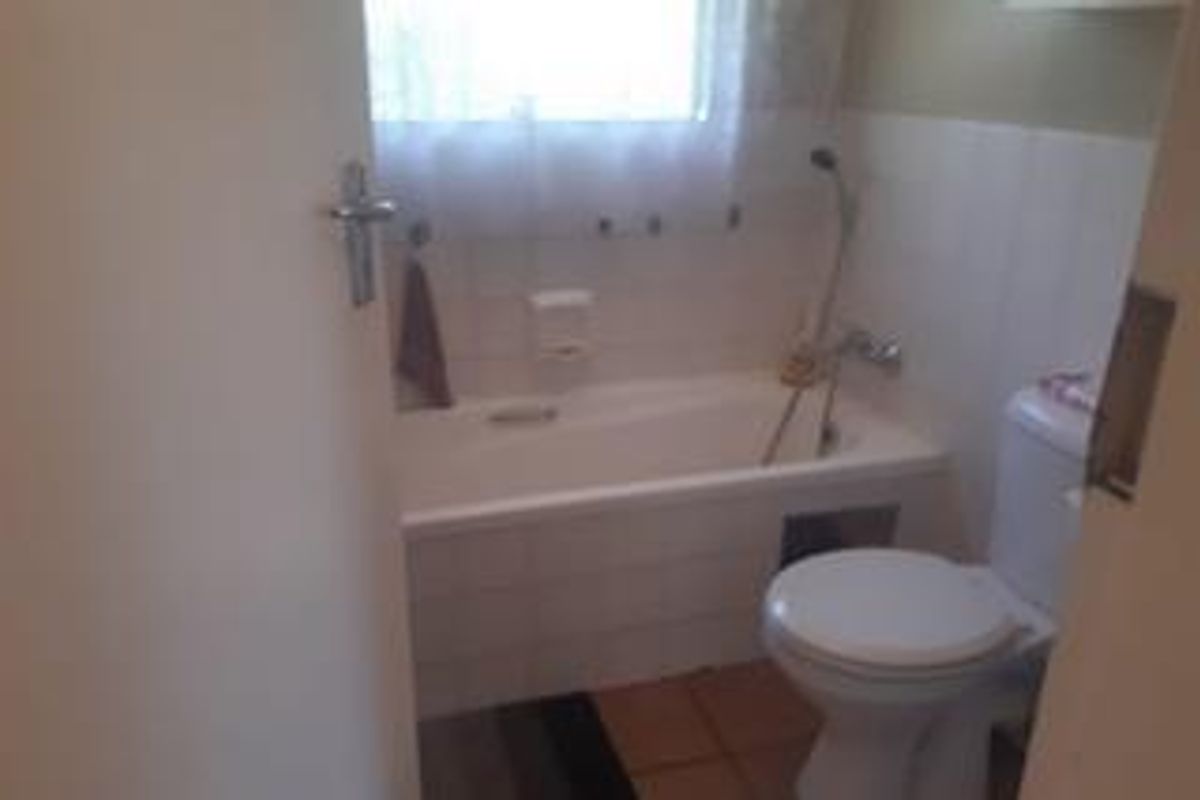 A functional bathroom featuring a bathtub with a handheld shower attachment and a standard toilet, finished with tiled walls and flooring.