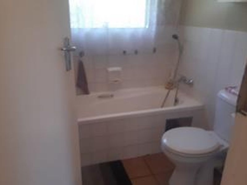 A functional bathroom featuring a bathtub with a handheld shower attachment and a standard toilet, finished with tiled walls and flooring.