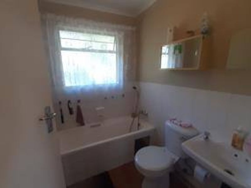 A functional bathroom featuring a bathtub, pedestal basin, and toilet, with dated finishes and wall-mounted storage, offering potential for modernization.