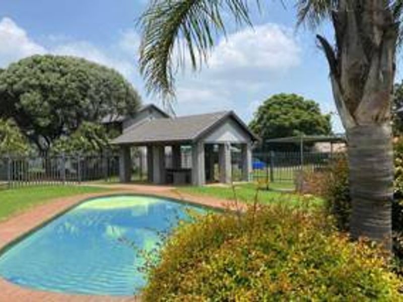 Outdoor pool area featuring a swimming pool with brick coping, a covered patio structure, and established garden landscaping within a fenced estate setting.