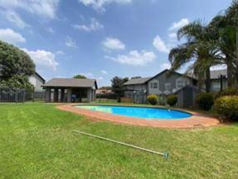 Communal outdoor area featuring a swimming pool, brick coping, and a covered gazebo set within a well-maintained garden space.