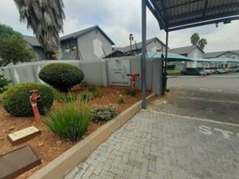 Entrance view of the townhouse complex featuring a paved driveway, security gate, and established garden landscaping.
