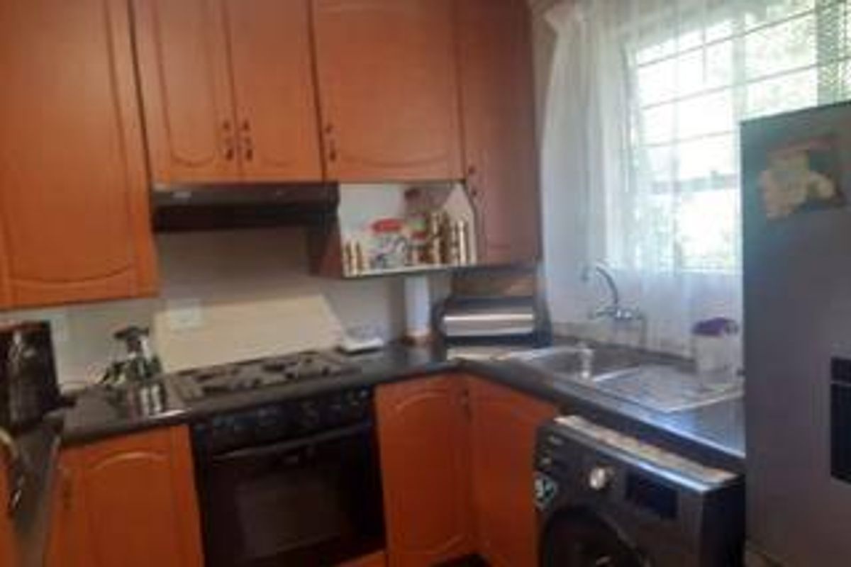 A functional kitchen featuring wood-finish cabinetry, a built-in oven with gas hob, extractor fan, and a double basin sink with a window view.