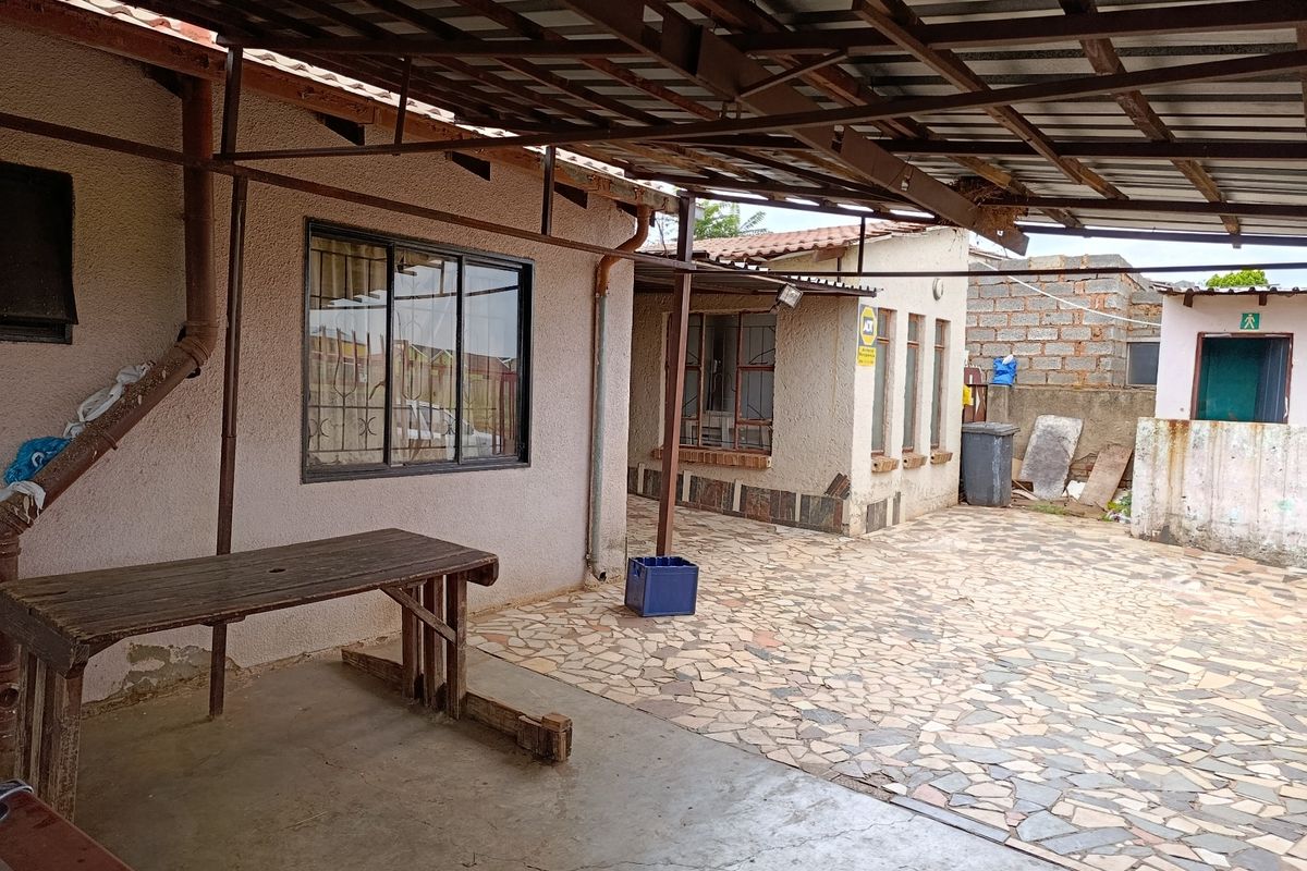 A covered outdoor patio area featuring paved flooring and a metal roof structure, showing signs of wear and requiring maintenance.