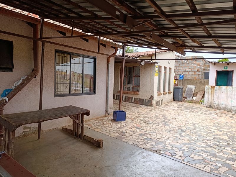 A covered outdoor patio area featuring paved flooring and a metal roof structure, showing signs of wear and requiring maintenance.