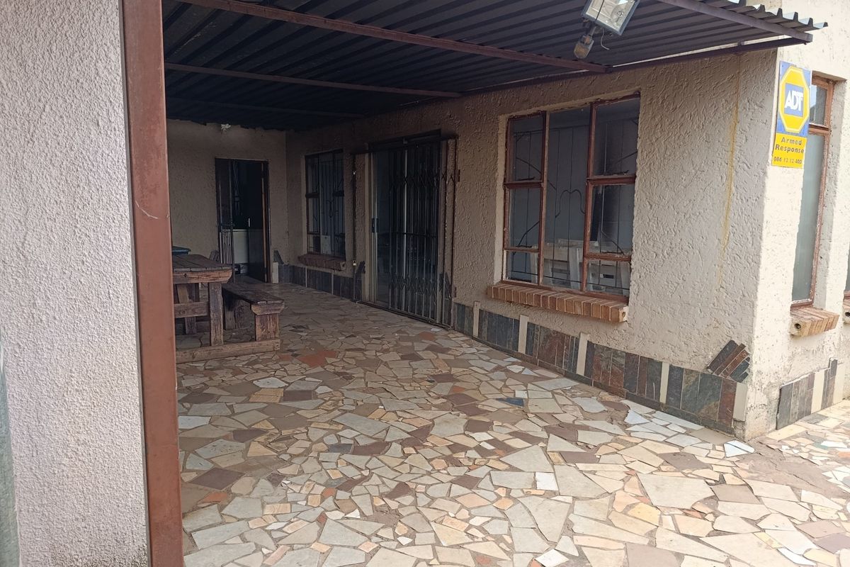 A covered outdoor patio area featuring crazy paving flooring, security gates, and metal roofing, providing a functional space for outdoor relaxation.
