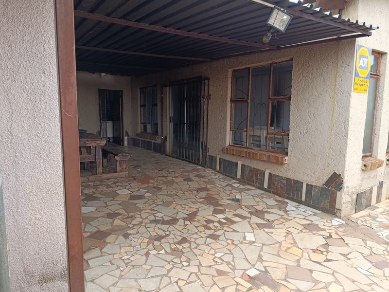 A covered outdoor patio area featuring crazy paving flooring, security gates, and metal roofing, providing a functional space for outdoor relaxation.