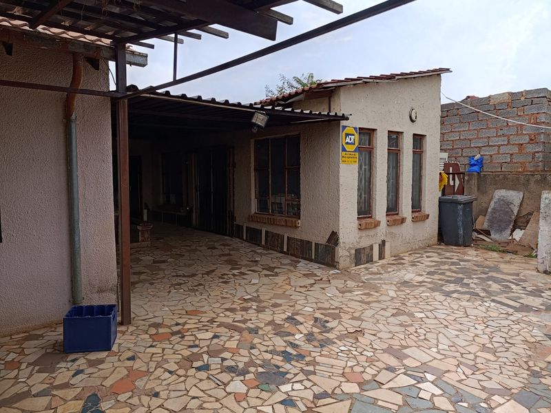 Rear exterior area featuring a covered patio with crazy paving flooring and weathered exterior walls.