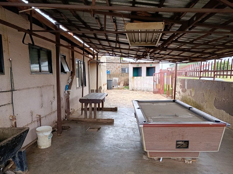 A covered outdoor patio area featuring a concrete floor, metal roofing structure, and external utility plumbing, requiring maintenance and cosmetic updates.