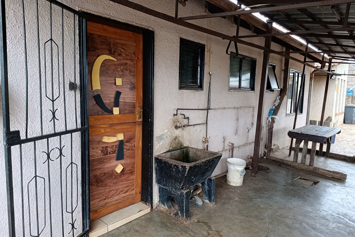 Covered outdoor utility area featuring a concrete sink, metal security gate, and direct access to the home via a wooden door.