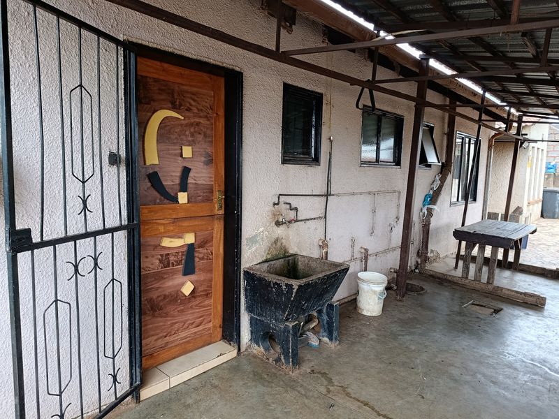 Covered outdoor utility area featuring a concrete sink, metal security gate, and direct access to the home via a wooden door.
