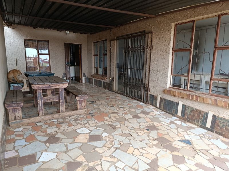 A covered patio area featuring crazy paving flooring, steel window frames with security bars, and a corrugated metal roof structure.