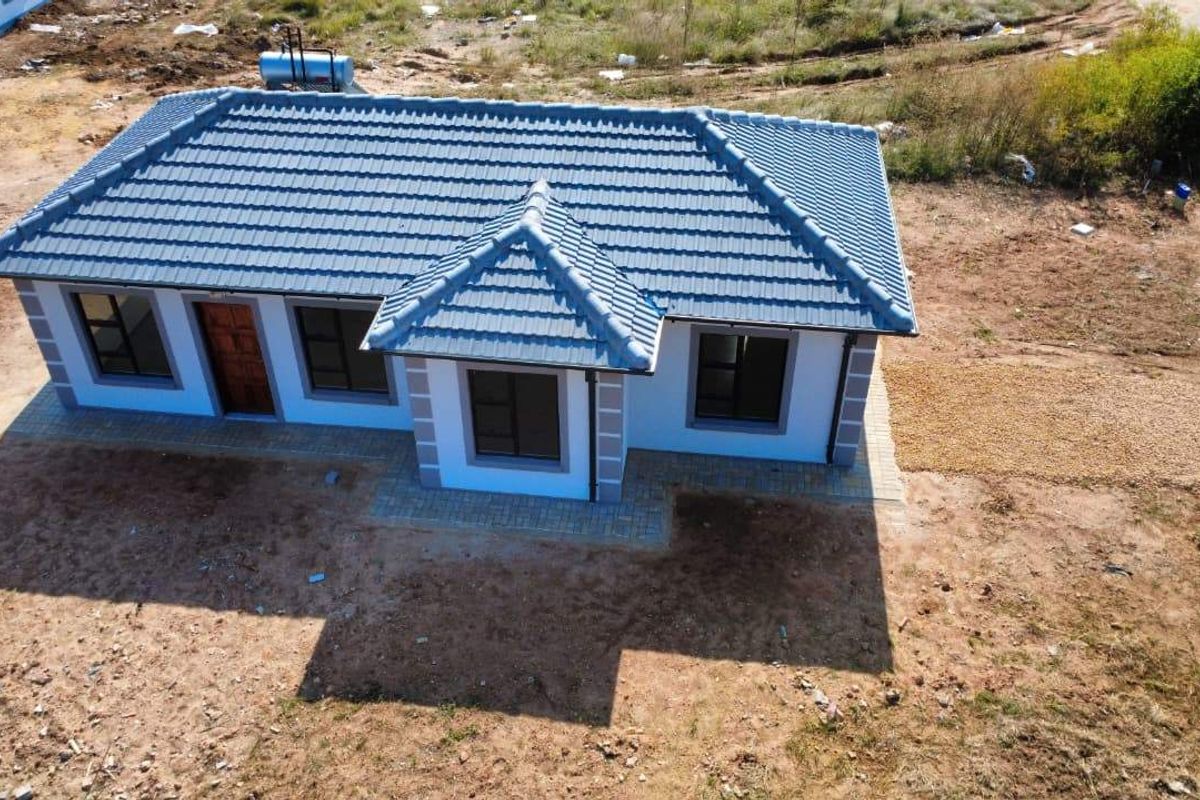 Aerial view of a newly constructed single-story house featuring a tiled roof, solar geyser, and paved entrance area on an unlandscaped plot.