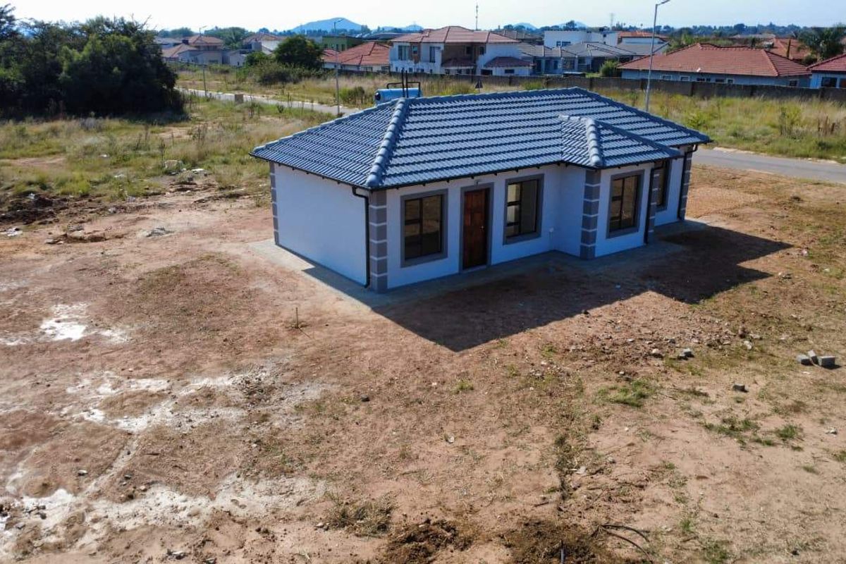 Aerial view of a newly constructed single-story house with a tiled roof, set on a large, undeveloped plot of land.