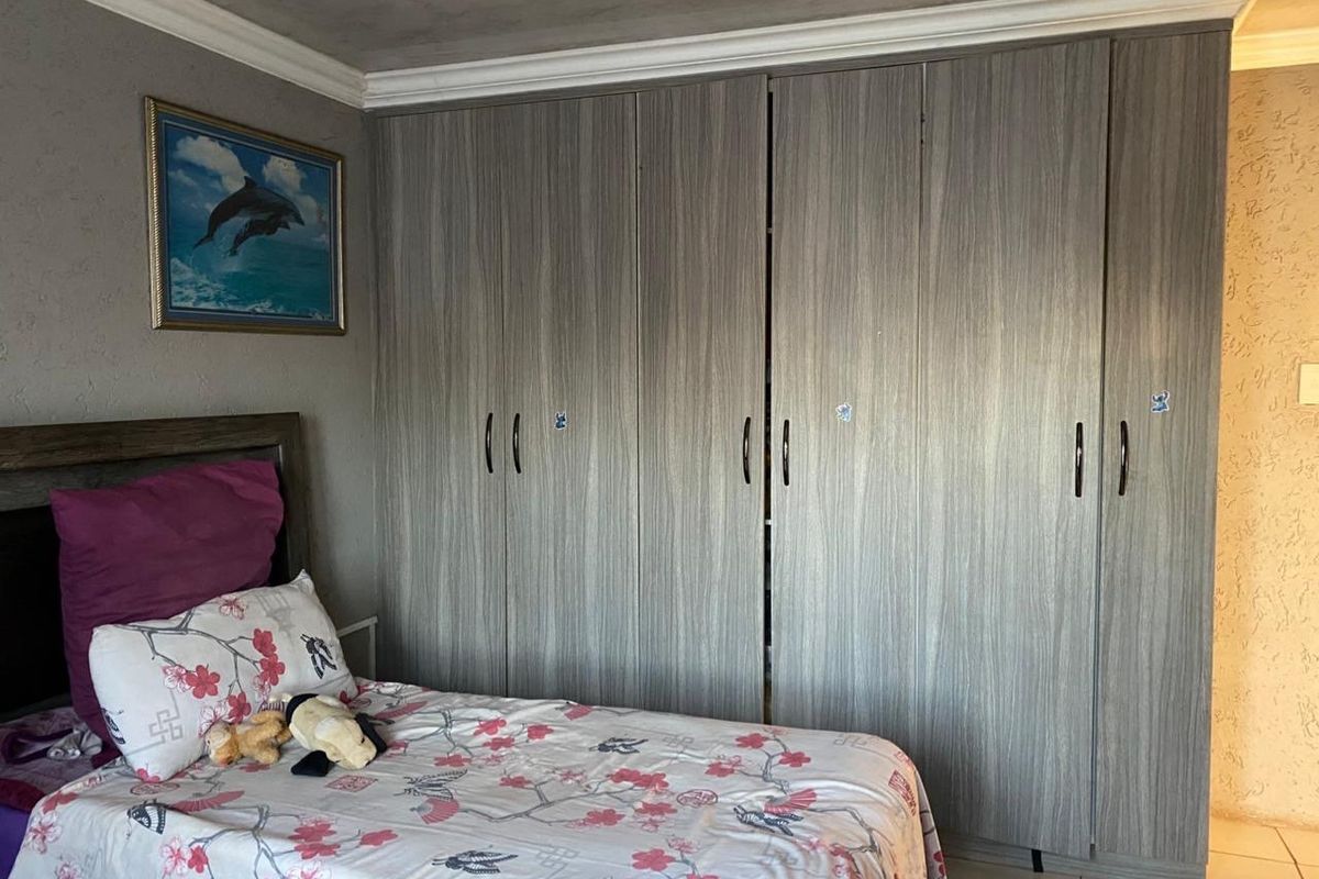 A bedroom featuring floor-to-ceiling built-in cupboards with a wood-grain finish, crown molding, and tiled flooring.