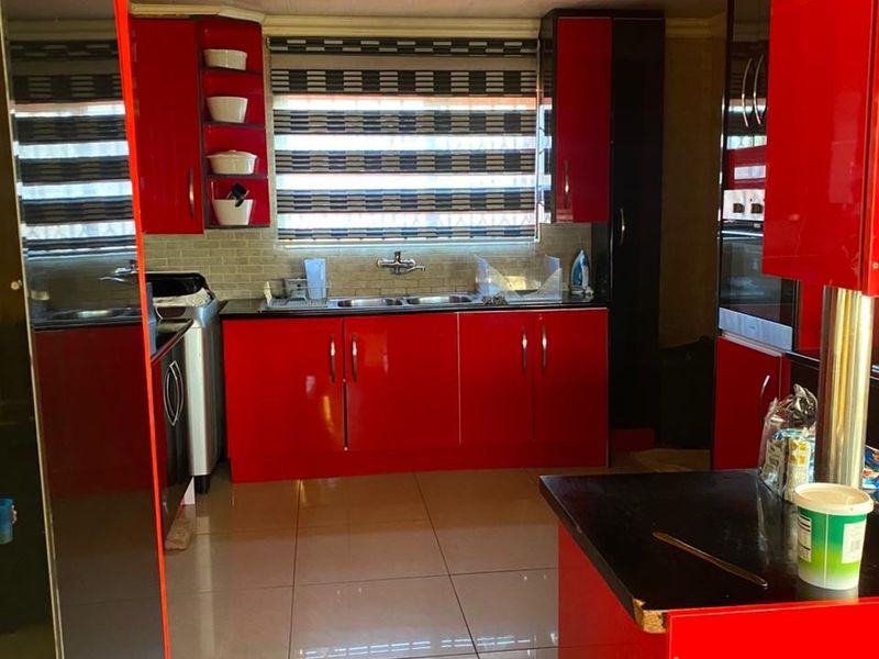 A vibrant kitchen featuring high-gloss red cabinetry, a double basin sink, tiled backsplash, and polished porcelain flooring with a modern drop ceiling design.