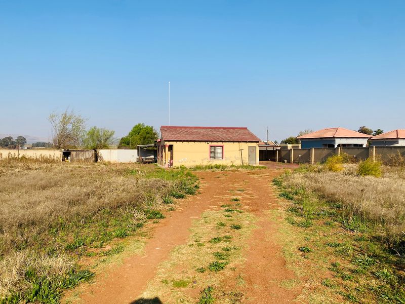 A detached single-story house featuring a tiled roof and perimeter wall, situated on a large plot with an unpaved driveway.