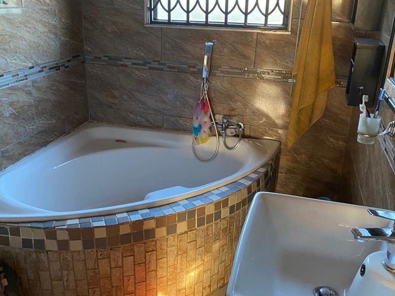 A bathroom featuring a corner bathtub with tiled surround, a modern basin, and a window fitted with security bars.