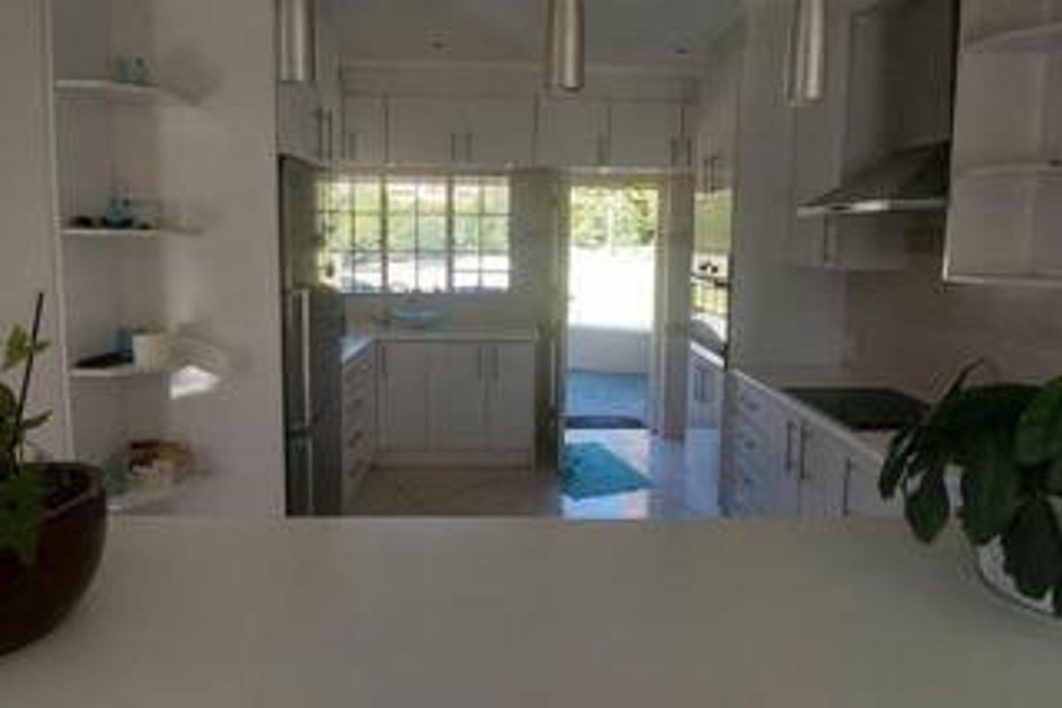A functional kitchen featuring white cabinetry, integrated appliances including a hob and oven, and a breakfast bar overlooking the workspace.