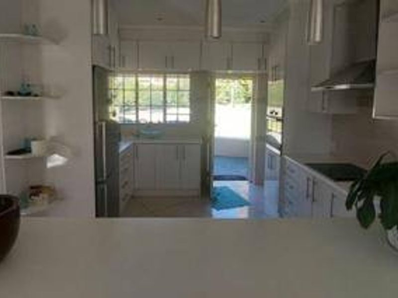 A functional kitchen featuring white cabinetry, integrated appliances including a hob and oven, and a breakfast bar overlooking the workspace.