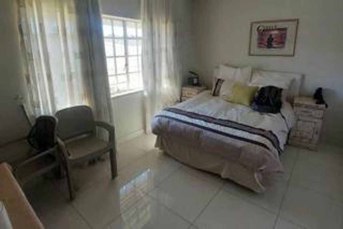 A bedroom featuring tiled flooring and a window with security bars, providing a functional and well-lit sleeping space.
