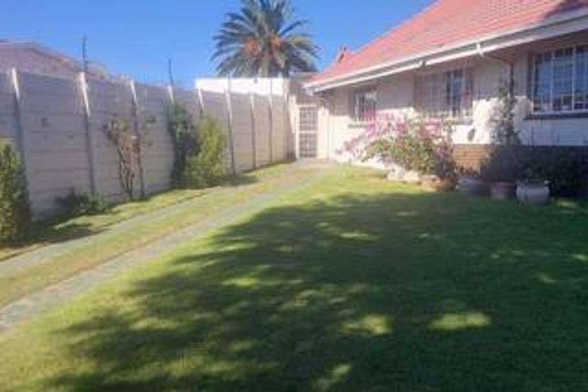 A rear garden area featuring a well-maintained lawn, paved driveway, and a secure precast concrete boundary wall.