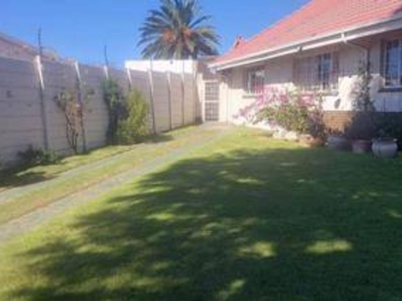 A rear garden area featuring a well-maintained lawn, paved driveway, and a secure precast concrete boundary wall.