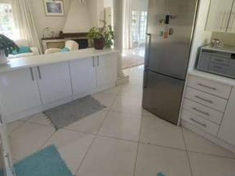 Open plan kitchen area featuring white cabinetry, a breakfast bar, tiled flooring, and integrated appliances, flowing into the adjacent living space.