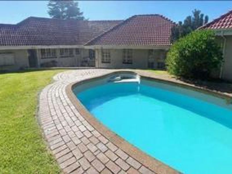 A backyard area featuring a swimming pool with brick paving surround and a view of the rear house elevation with tiled roofing.