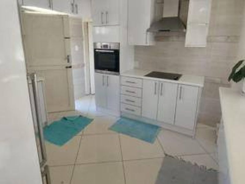 A functional kitchen featuring white cabinetry, a built-in oven, an electric hob with an extractor fan, and tiled flooring.