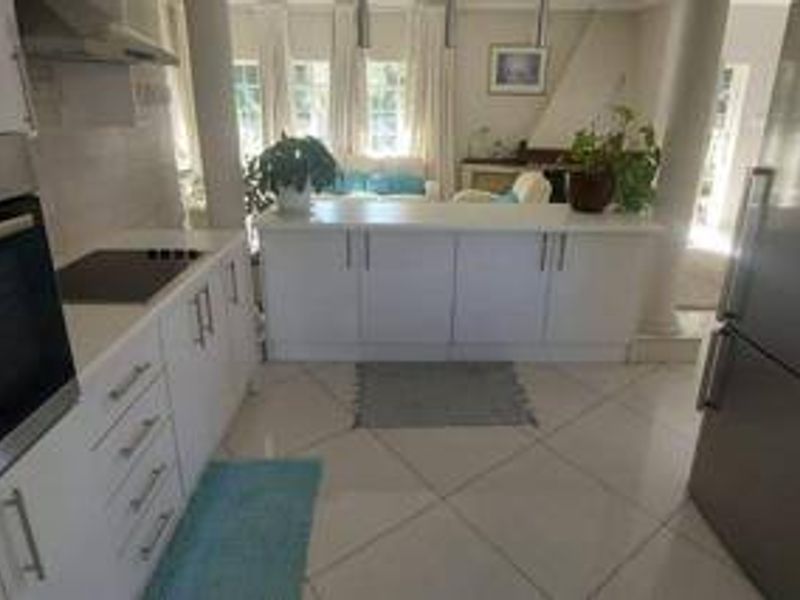 Open-plan kitchen featuring white cabinetry, stone countertops, built-in oven, and electric hob, seamlessly flowing into the adjacent living area with tiled flooring.