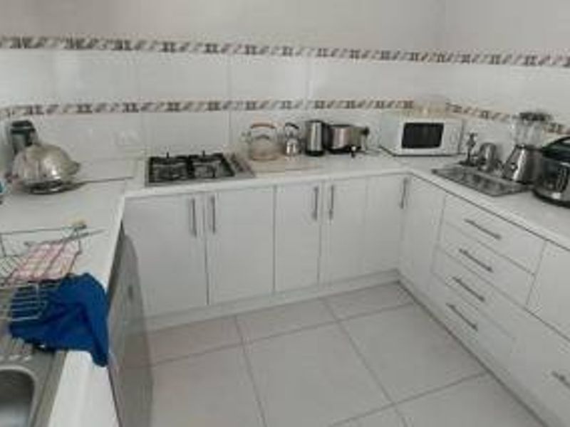 A functional kitchen featuring white cabinetry, a gas hob, tiled backsplash, and tiled flooring, providing a clean and practical workspace.