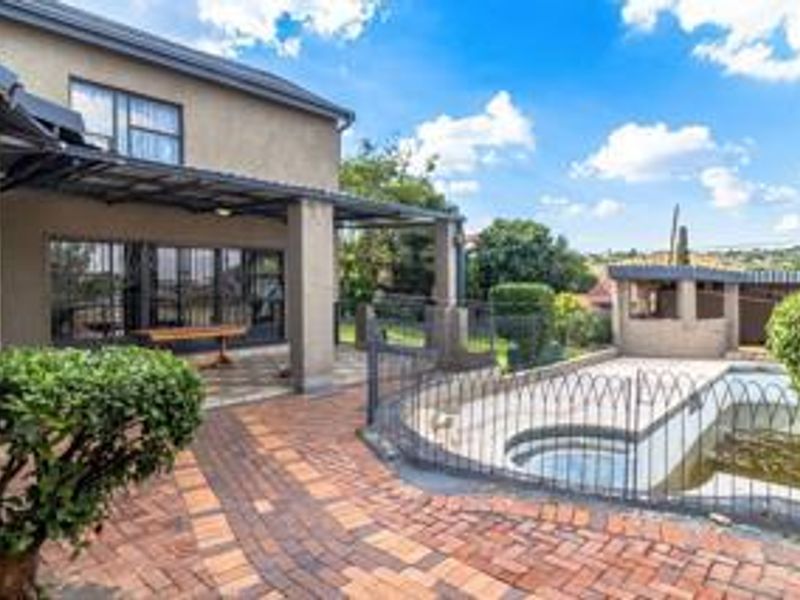 Rear exterior view featuring a covered patio, paved courtyard area, and a swimming pool with security fencing.
