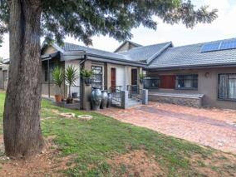 Front elevation of a single-story house featuring a tiled roof with solar panels, a brick driveway, and secure window treatments.