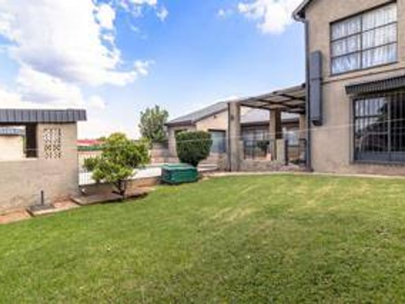 Rear view of the property featuring a lawn, a covered patio area, and security bars on the windows and doors.