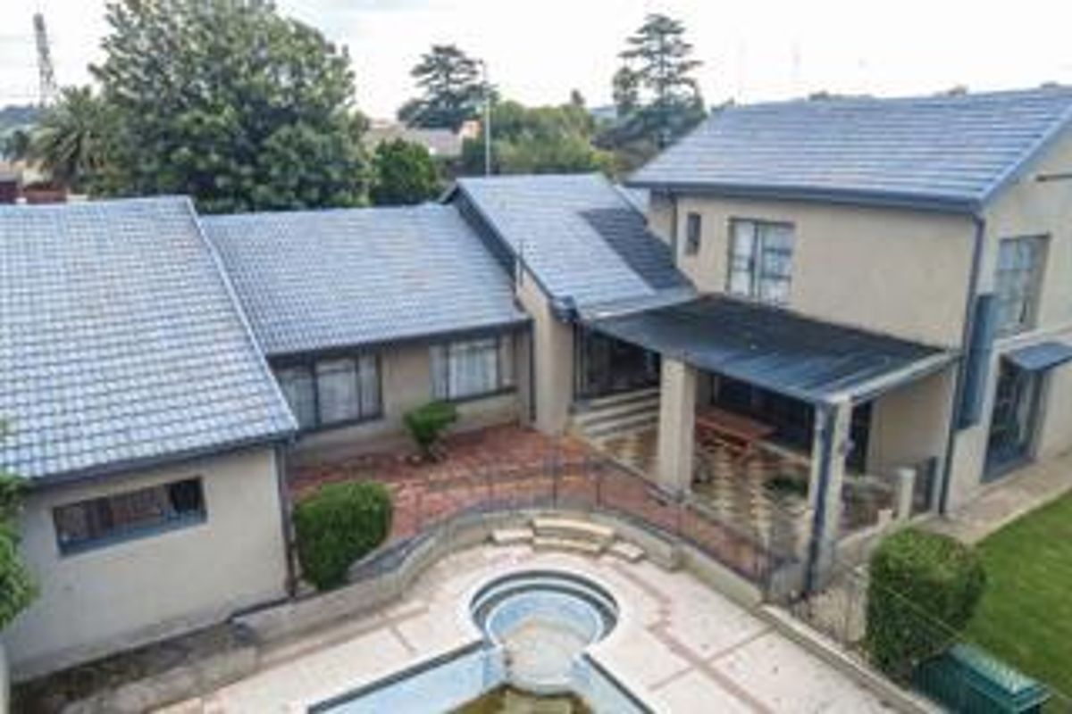 Aerial view of the rear exterior featuring a swimming pool, paved courtyard area, and a covered patio attached to the main house structure.