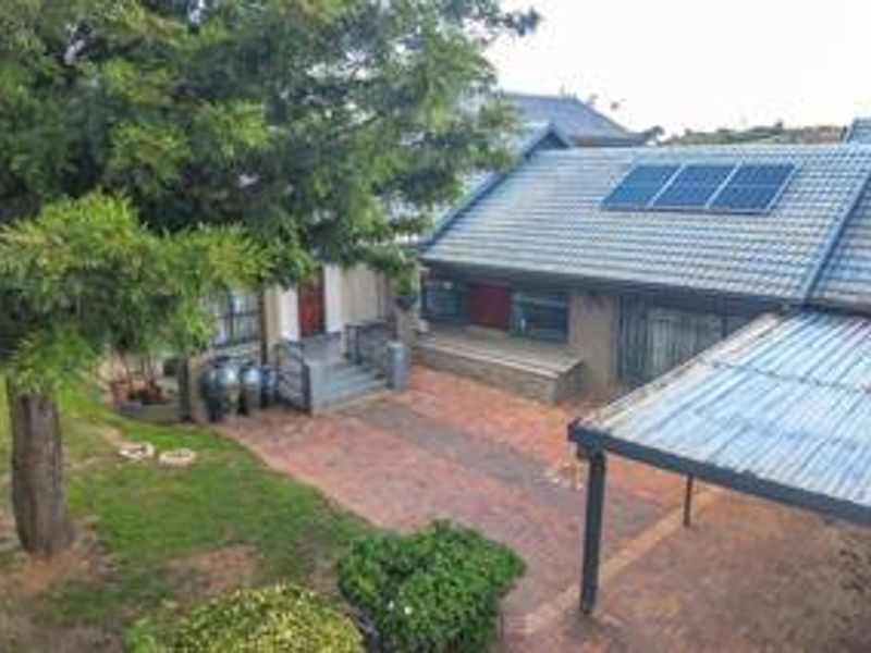 Rear exterior view featuring a paved courtyard, covered patio area, and a tiled roof equipped with solar panels.