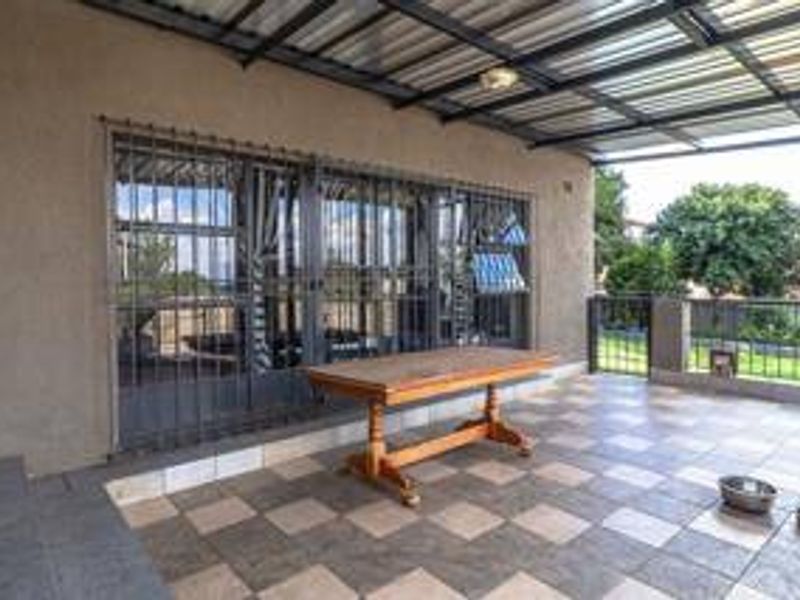 A covered outdoor patio area featuring tiled flooring, a metal roof structure, and secure sliding glass doors leading into the home.