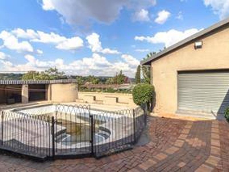 Outdoor pool area featuring a fenced swimming pool, brick paved patio, and a garage with a roller shutter door.
